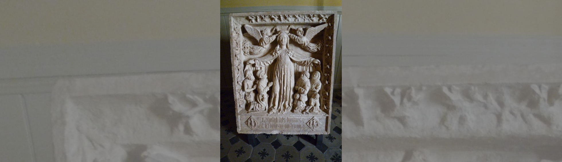 Ce bas relief évoque l'hospice des tisserands(tixadors): une vierge abrite sous son large manteau ouvert les malades agenouillés