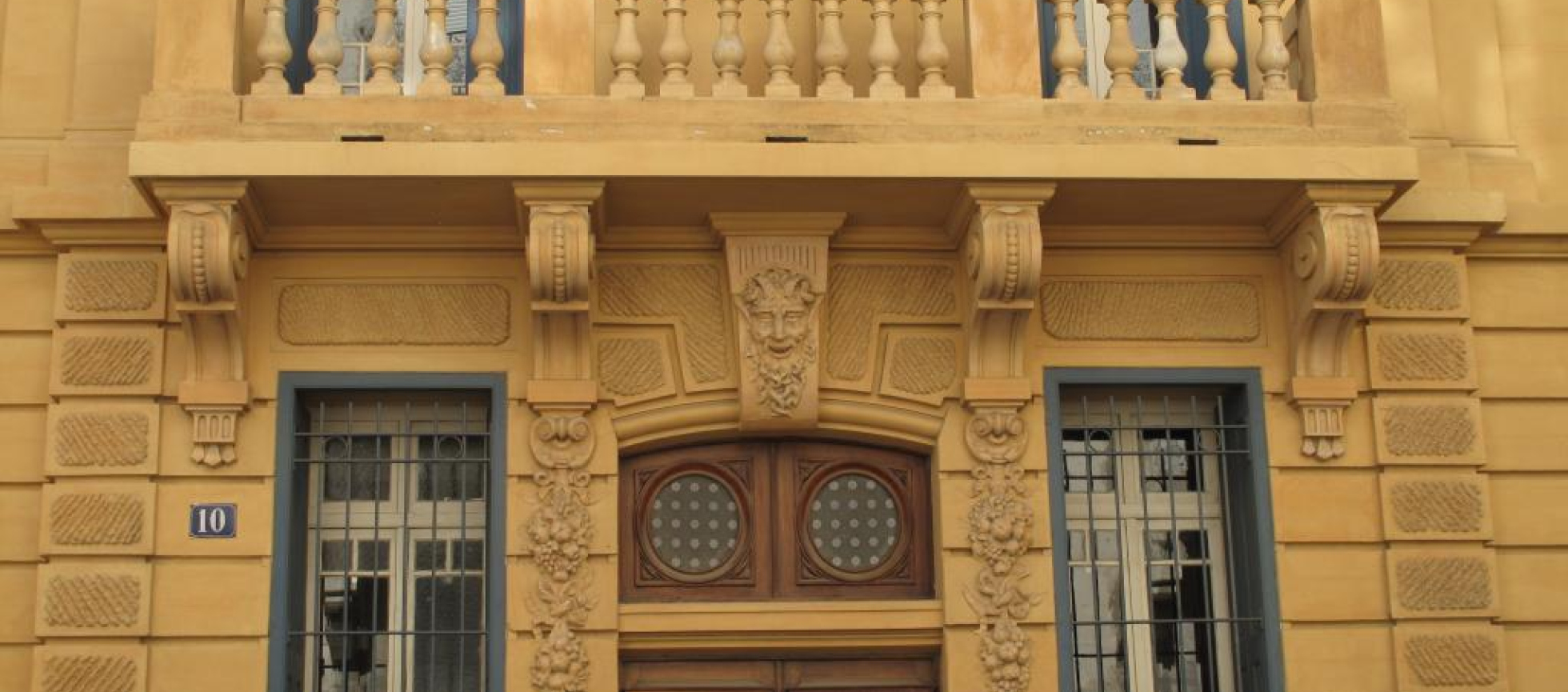 Façade peinte en ocre jaune ,balcon à balustres au 1er,guirlandes et tête de faune ornant les piedroits et linteau de l'entrée